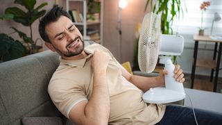Man struggling in hot weather, holding a desktop electric fan close to himself