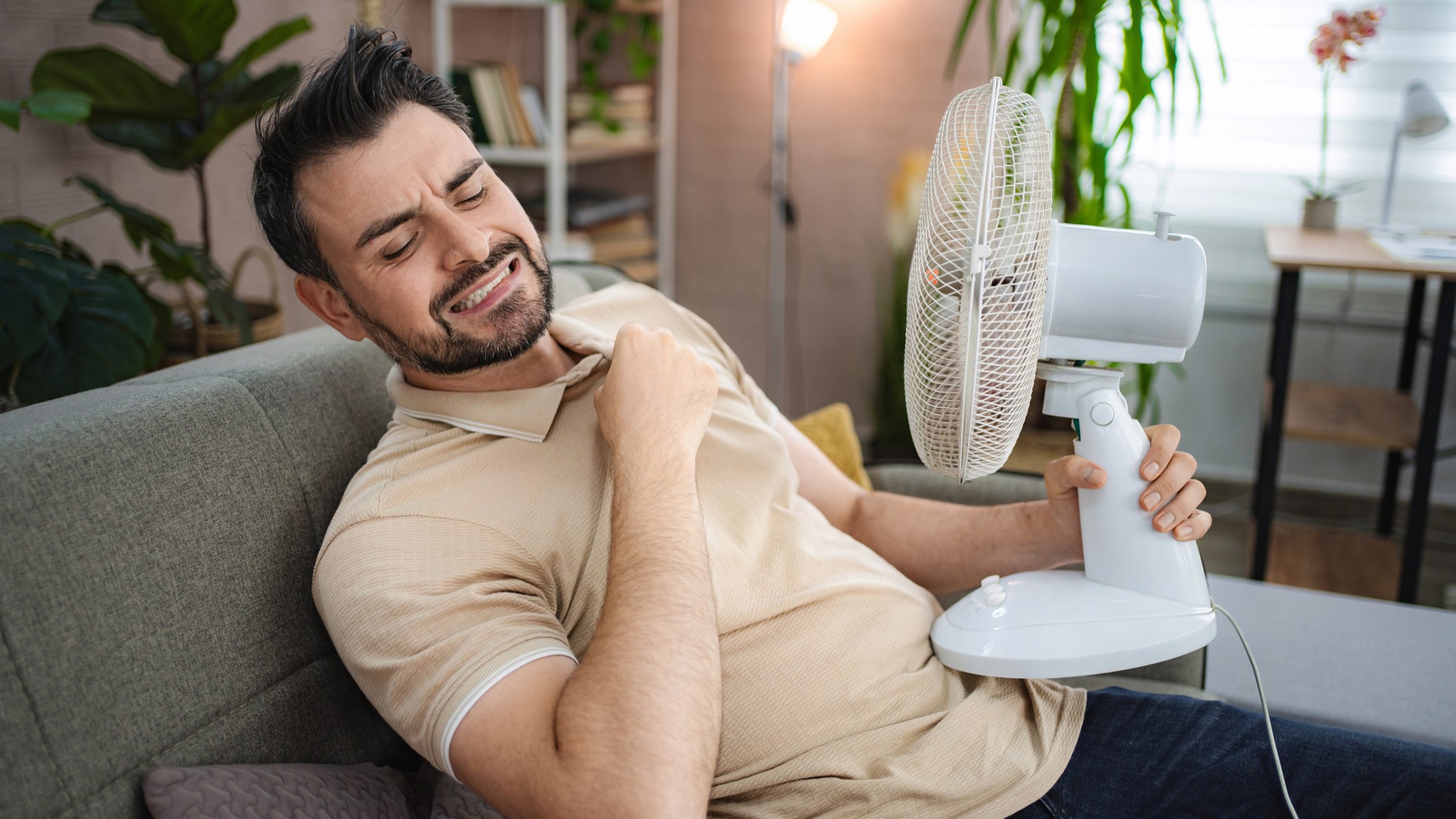 Man struggling in hot weather, holding a desktop electric fan close to himself
