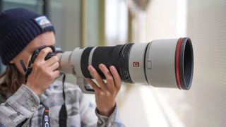 A picture of a man holding the Sony A7R VI camera with the Sony 100-400mm f/4.5 GM lens mounted. The camera is being held up to the man's eye while he takes a picture.
