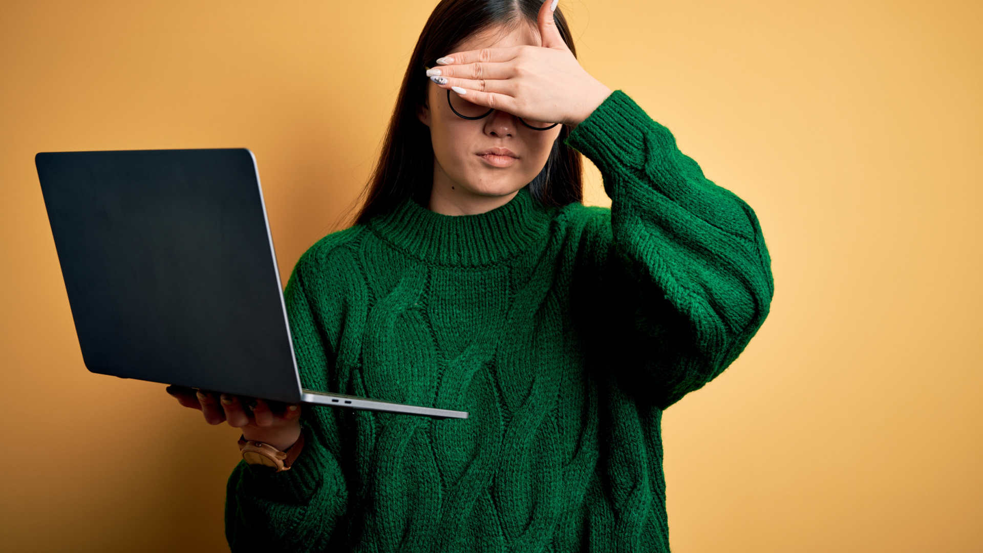 Young asian business woman wearing glasses and working using computer laptop covering eyes with hand, looking serious and sad.