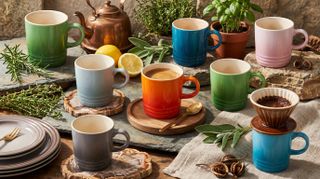Collection of multicolored Le Creuset mugs with coffee making equipment and herbs