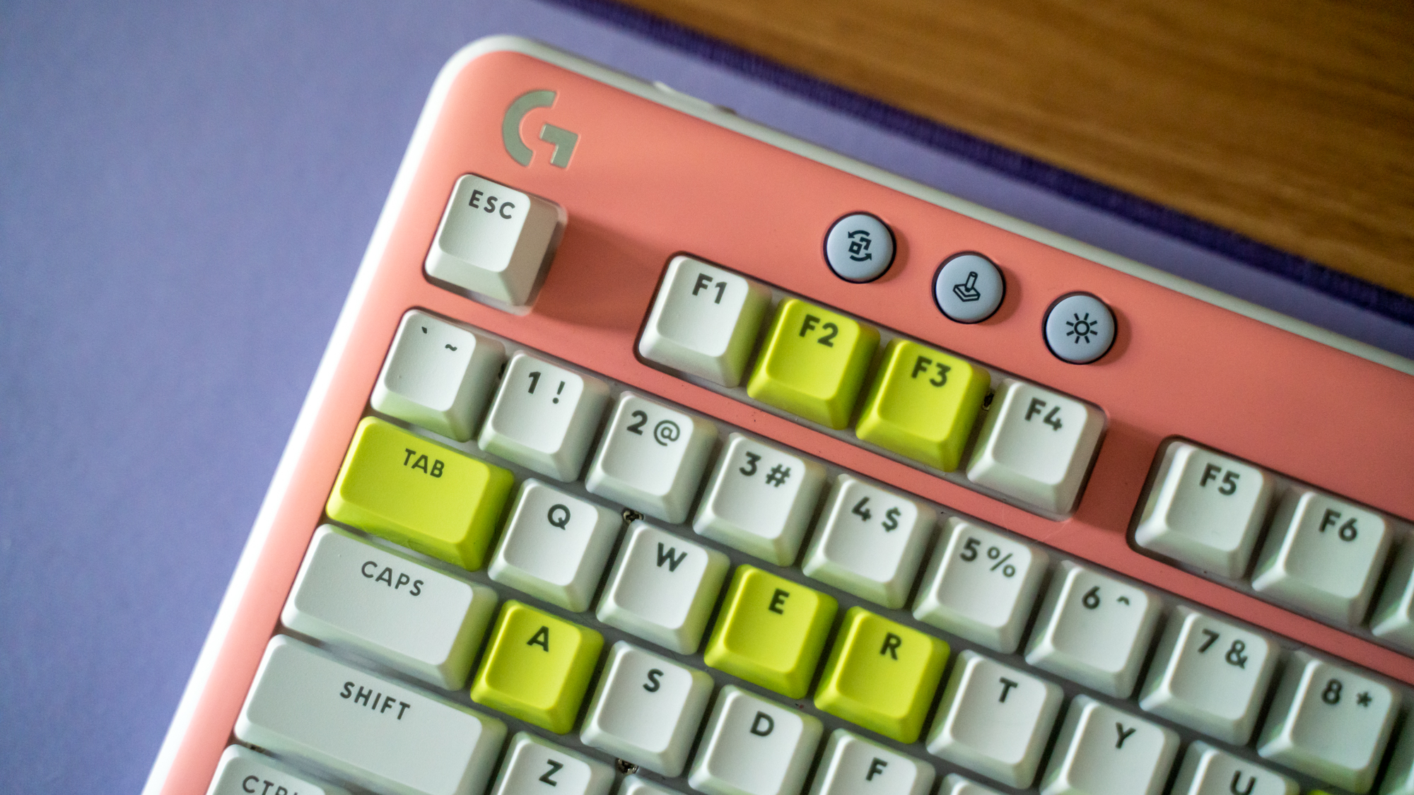 Logitech G715 TKL in its pink deck cover and white and green keys on purple Logitech desk mat