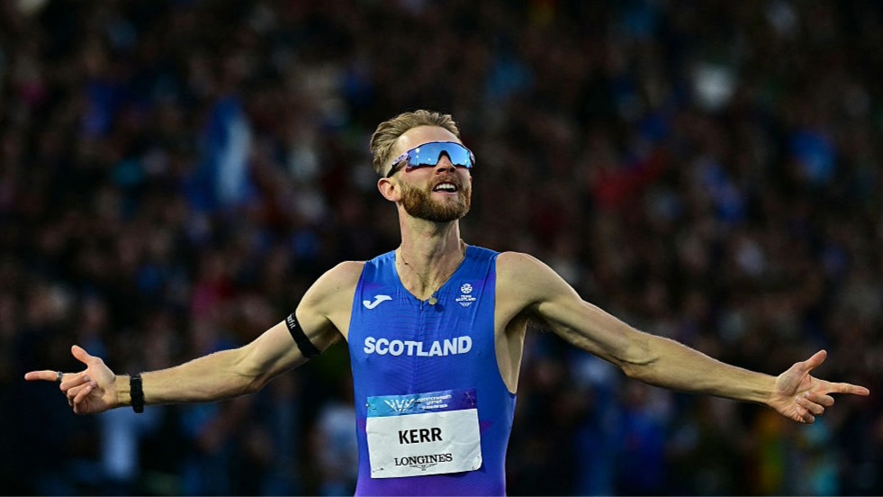 Josh Kerr, wearing sunglasses and the Scotland vest, holds his arms out in celebration at winning the mile at the Commonwealth Games 2026.