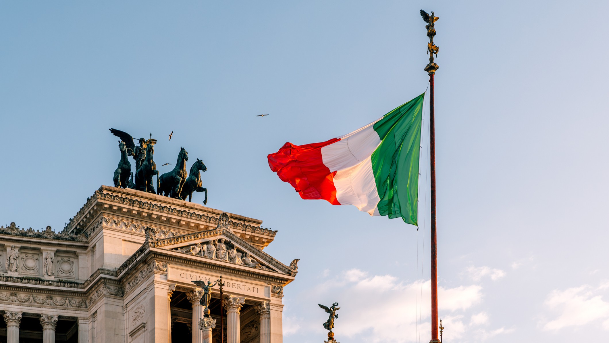 Italian flag waving in the wind and Altare Della Patria in the background, Rome, Italy