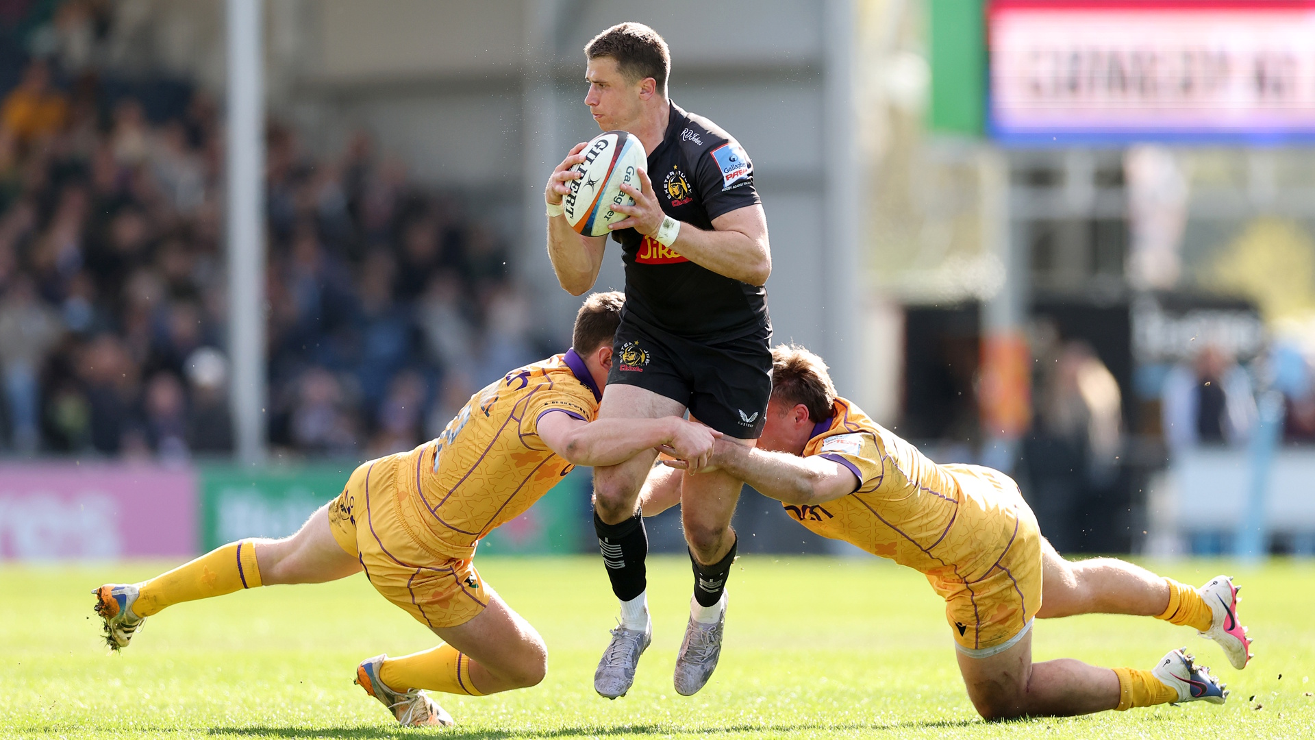 Harvey Skinner of Exeter Chiefs is tackled by Fraser Dingwall and Tom Litchfield of Northampton Saints during the Gallagher PREM match between Exeter Chiefs and Northampton Saints in 2026.
