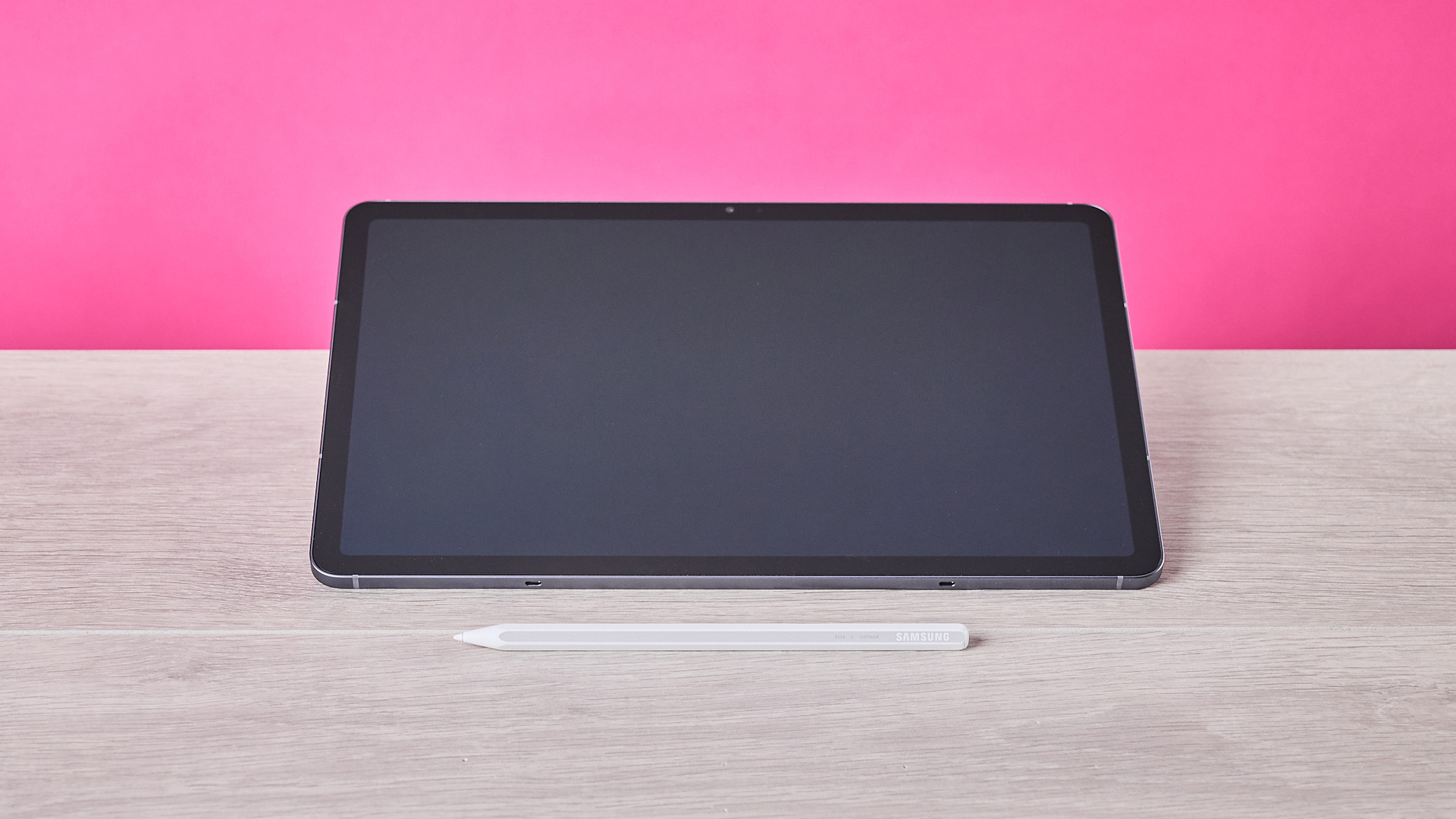 Front view of Samsung Galaxy Tab S11 and S Pen, on a desk with pink wall in background