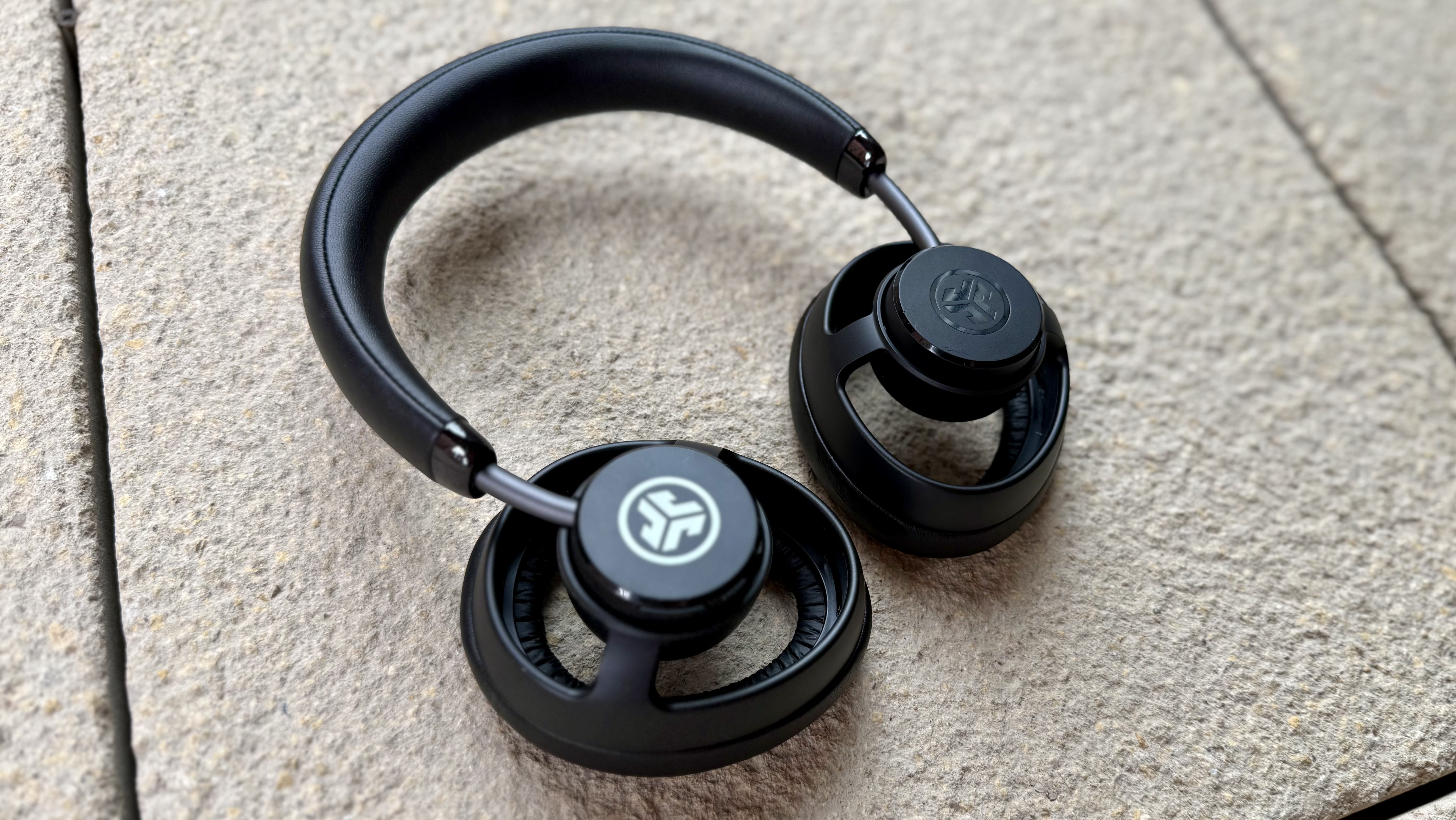 The jlab jbuds open headphones pictured on a stone surface with their grilles removed