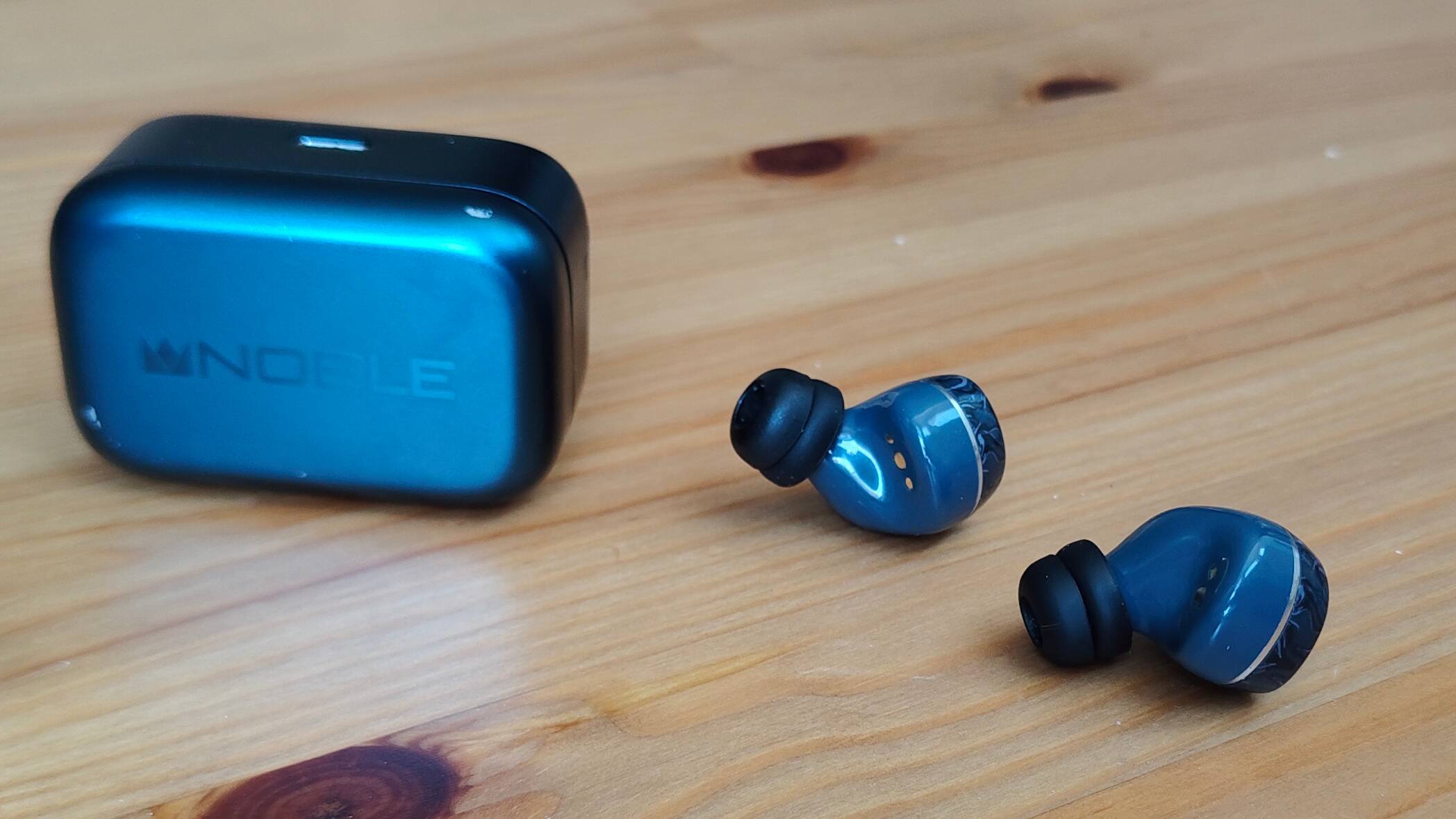 The Noble Osprey earbuds, on a table next to the case.