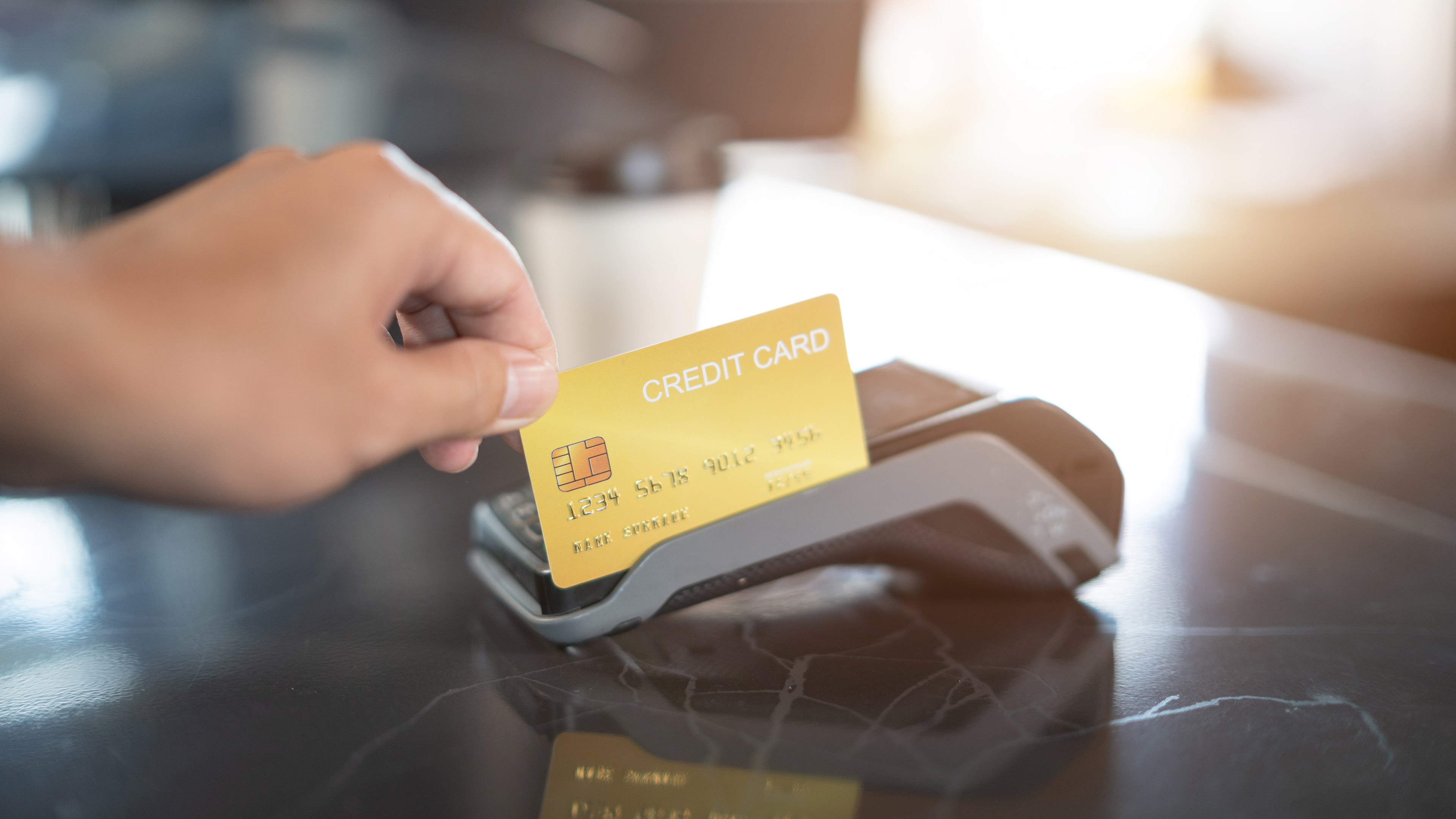 A hand swiping a credit card in a payment terminal on a counter