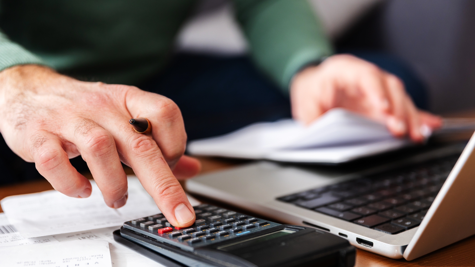 Close-up view of man calculating expenses and managing the budget while using a calculator and laptop at home