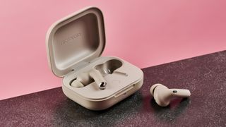 The Motorola Moto Buds Plus case is sitting open, with the left earbud inside, and the right earbud sitting outside of the case on a dark surface. The charging case is pictures against a dark background.
