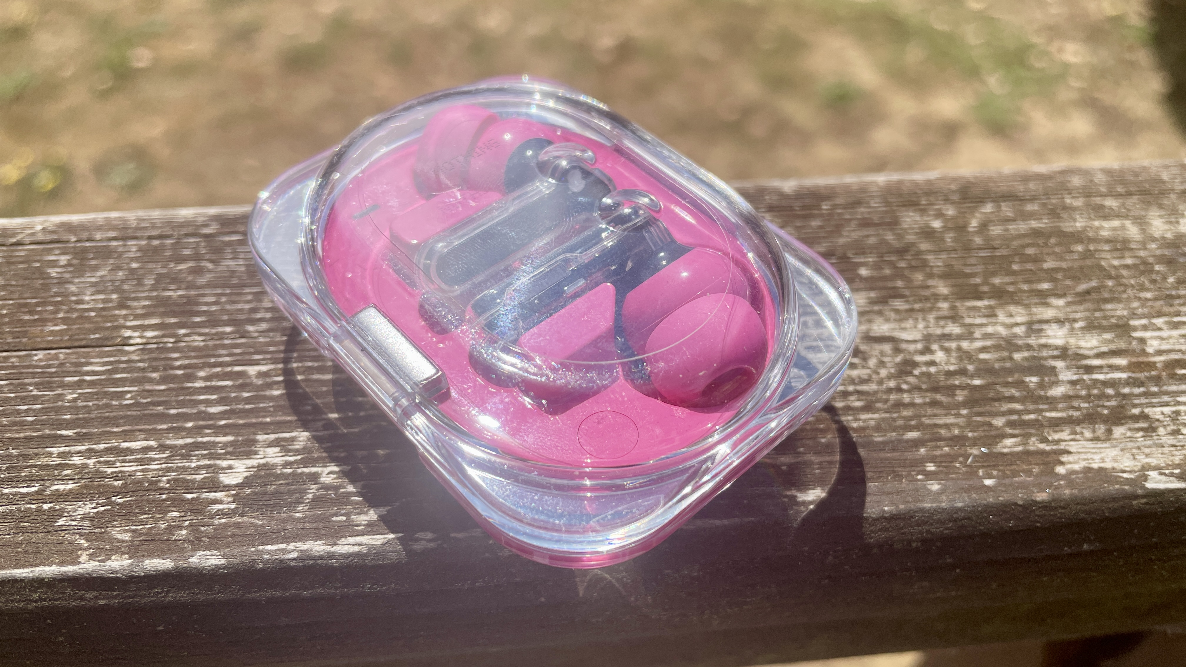 Nothing Ear (3a) in their case, on a sunny day, on a wooden rail