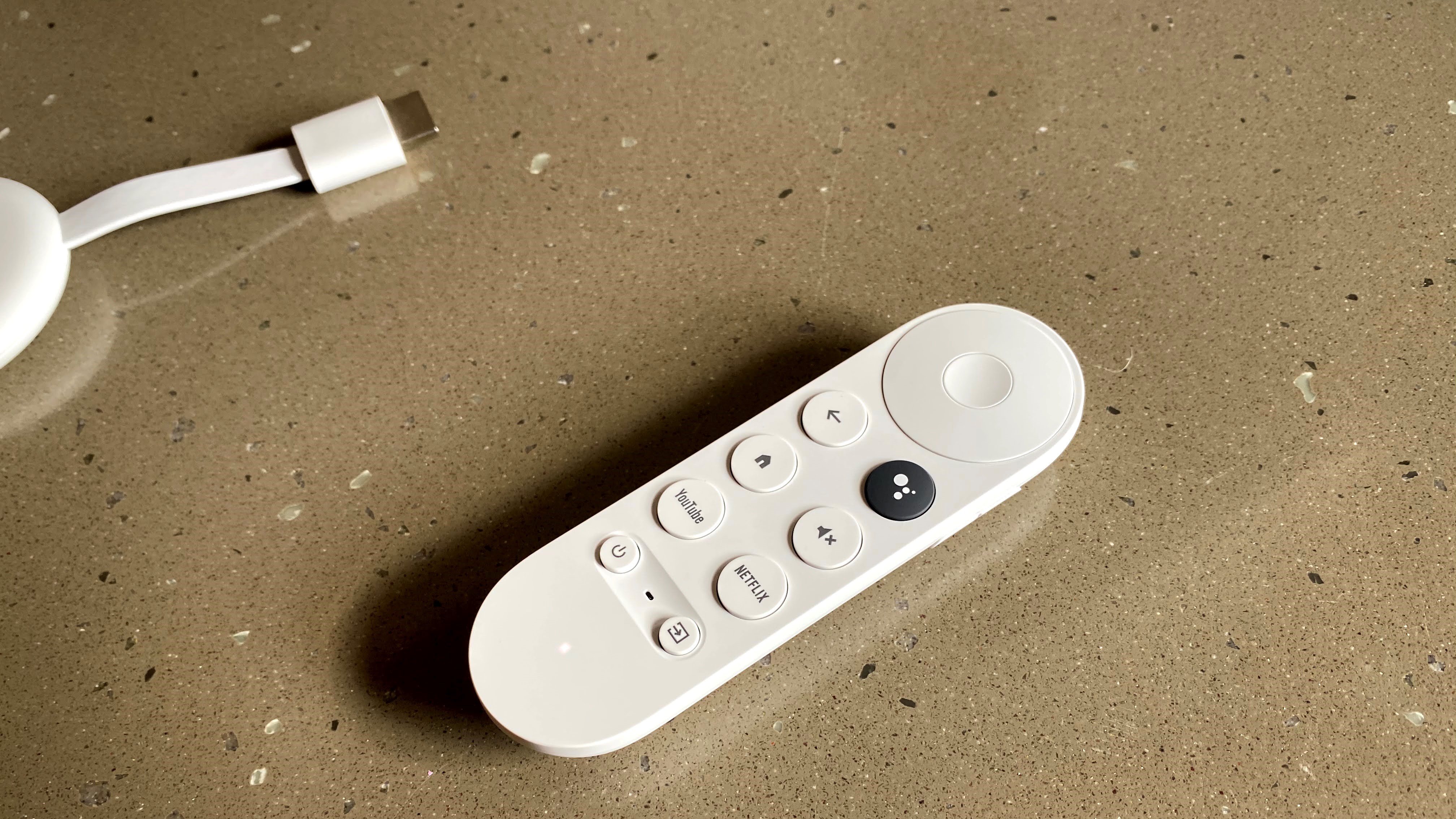 The Chromecast with Google TV remote in white on a grey surface.