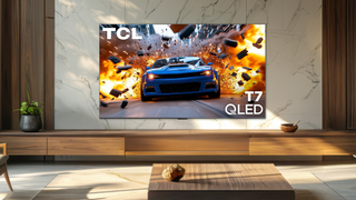 Promotional image of the TCL 7 Series in a neutrally decorated daytime room with a rendered image of a fast car and explosions on the screen
