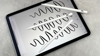 The Apple Pencil USB-C, Metapen Pencil Air8, and ESR Geo Digital Pencils are pictured lying on an iPad, which is displaying squiggly lines from each pencil.