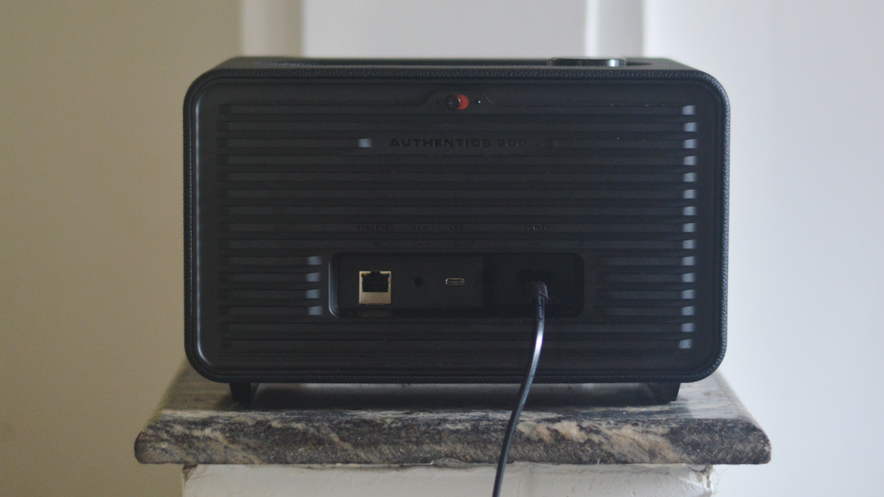 The JBL Authentics 200 speaker on a sits on a small marble surface. We can see its rear, including power and internet connection ports.