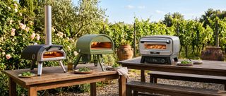 Three pizza ovens on wooden tables outside in a garden