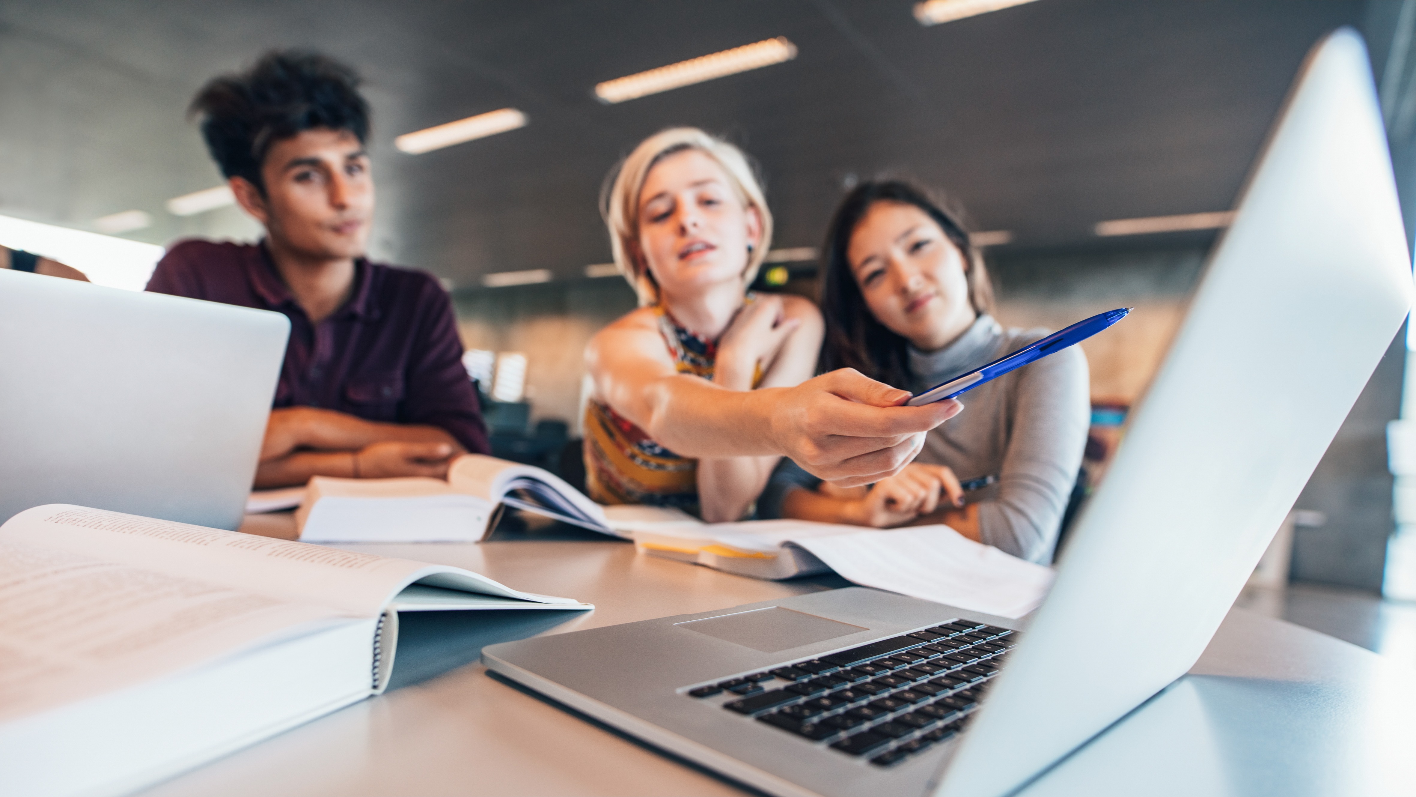 Multiracial young people doing group study at table with woman pointing at laptop. University students researching information for their project.