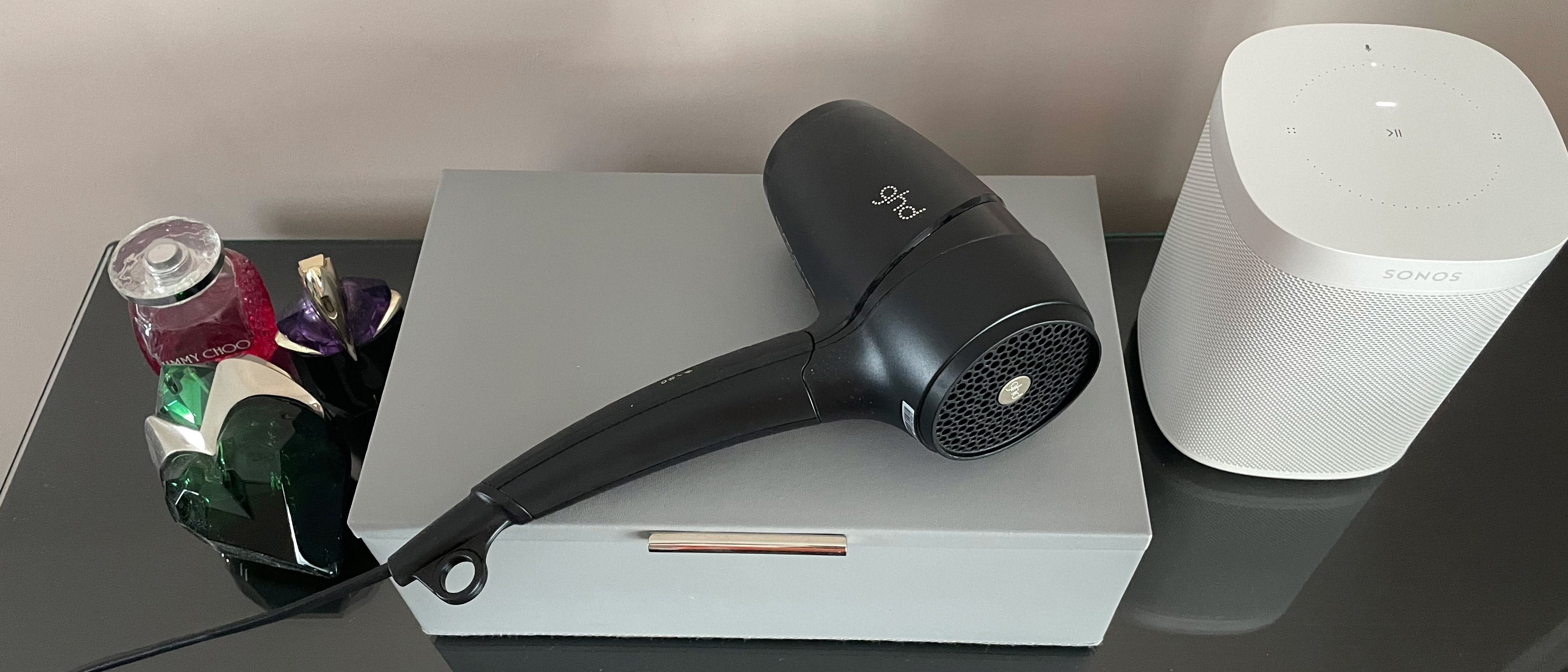 The GHD Flight hair dryer resting on a grey leath jewellery box on a glass dressing table