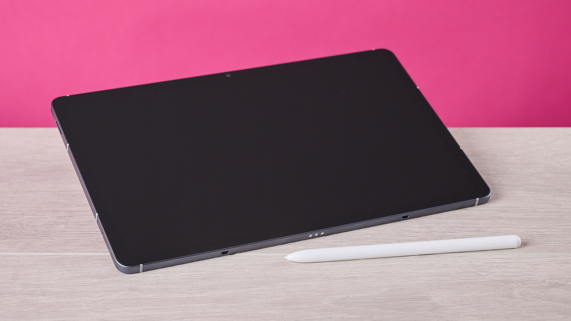 The Samsung Galaxy Tab S10 FE sat at an angle on a table behind the S Pen and in front of a pink background.