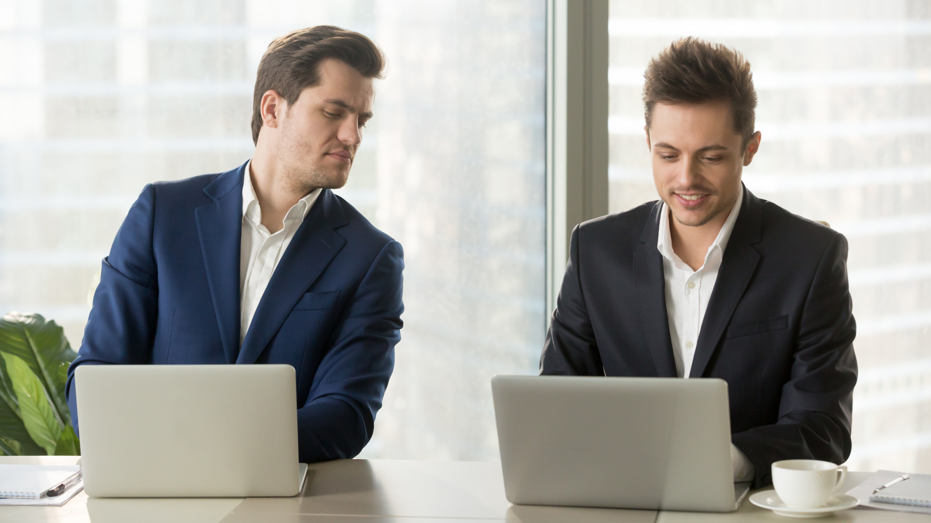 A man copying from the laptop screen of his colleague