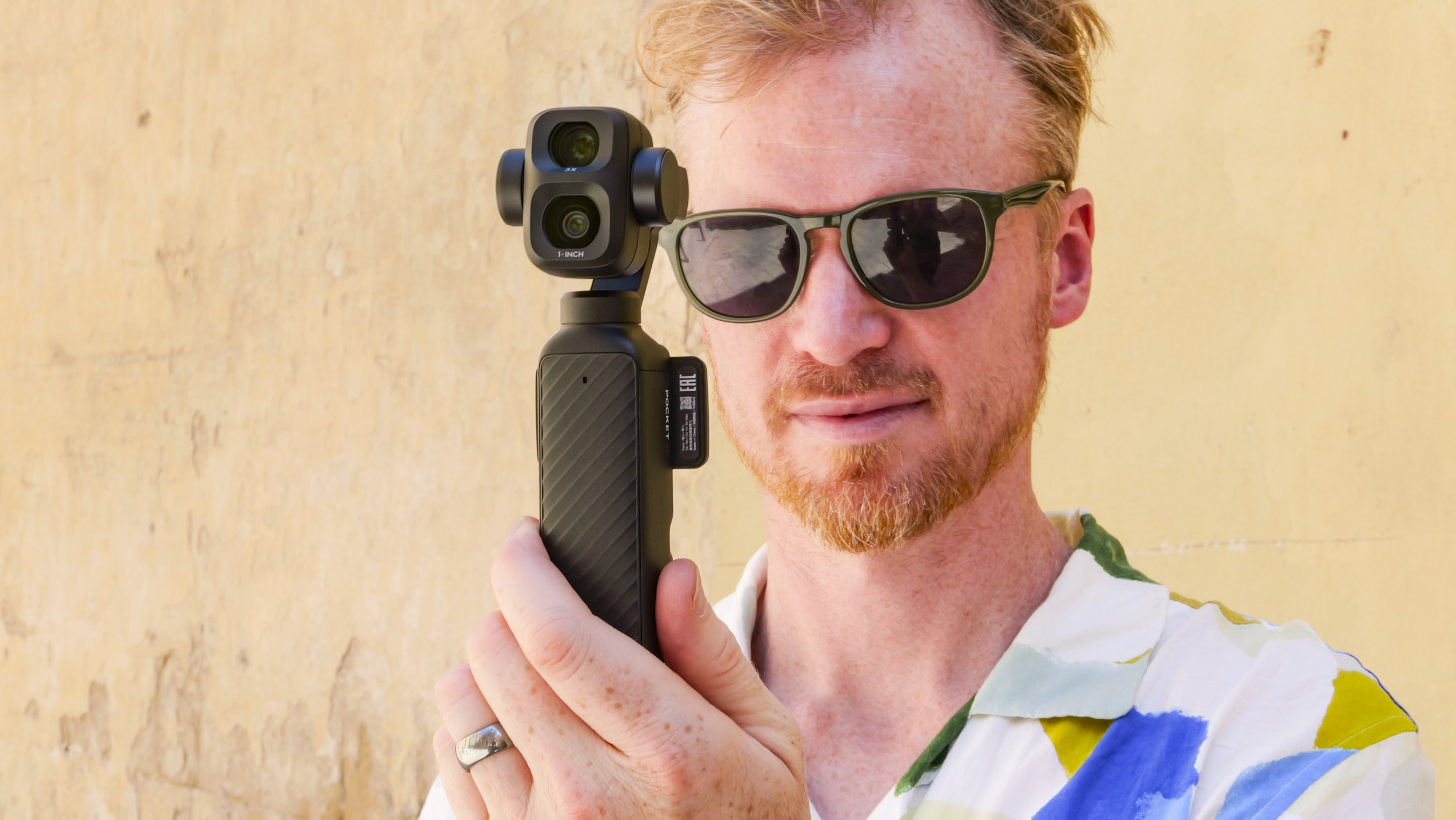 Man in bright summer short and shades, in an old town on a sunny day, holding the DJI Osmo Pocket 4P vlogging camera