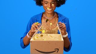 A woman opening a brown box with the Amazon logo on it as various gold and sparkly items explode out of it.