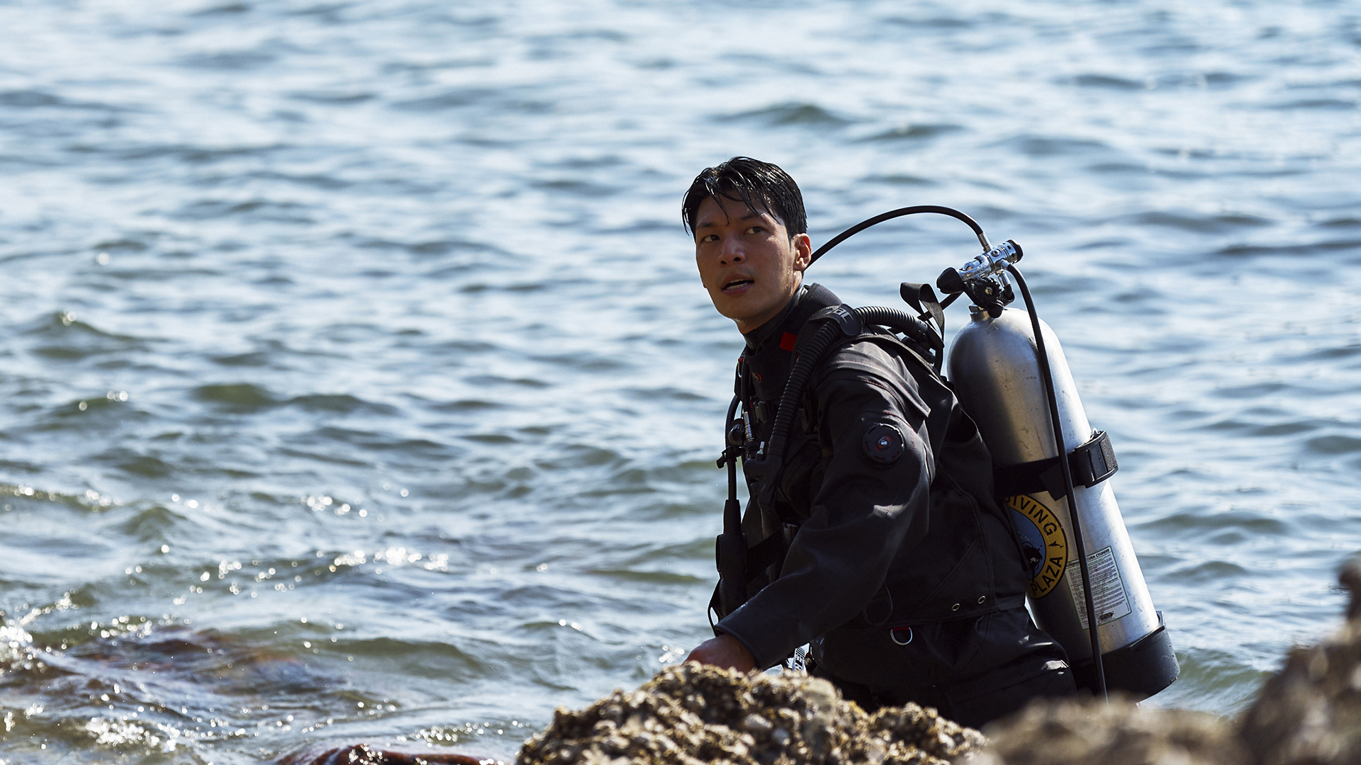 Jun-ho sitting on a rocky shore with his diving suit and equipment on in Squid Game season 3