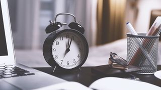 An image of an alarm clock on a desk next to a laptop