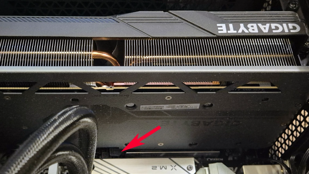 A graphics card inside a PC case with a red arrow pointing at the PCIe slot release lever beneath it
