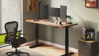 A PC and two monitors sitting atop a FlexiSpot E7 frame Bamboo series standing desk in an office with an office chair and cabinet