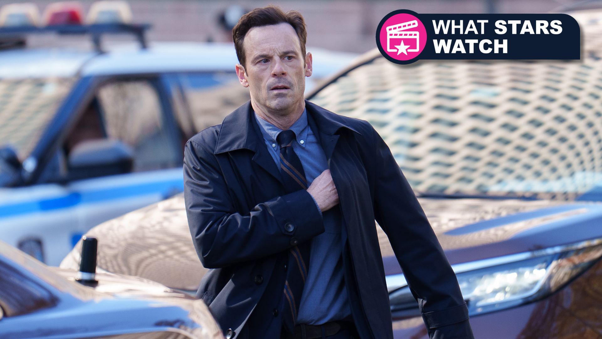 Danny walks in front of a car while getting something out of his inside jacket pocket