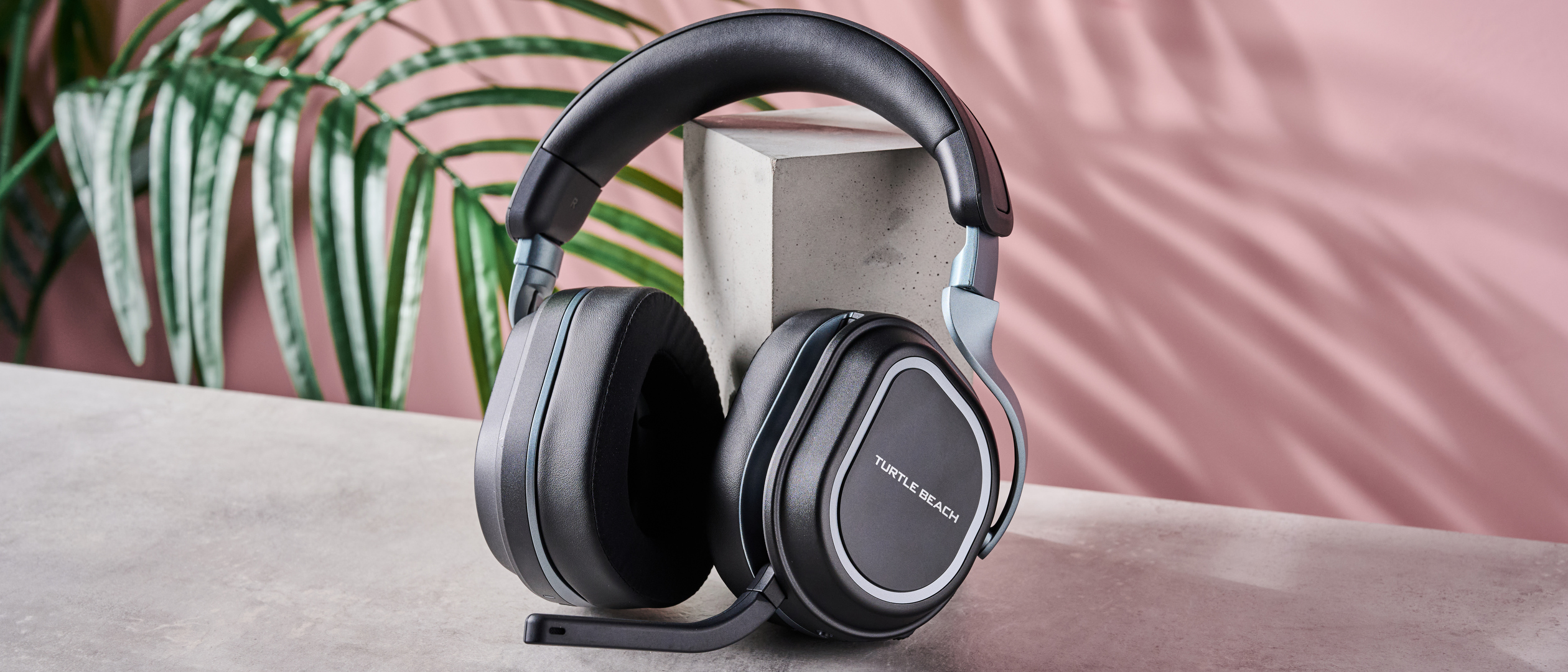 Turtle Beach Stealth 700 Gen 3 leaning on plinth, on desk with plant and pink wall in background