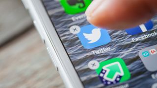 Close up to finger deleting the Twitter app on the screen of an iPhone 7 Plus with personalized background.