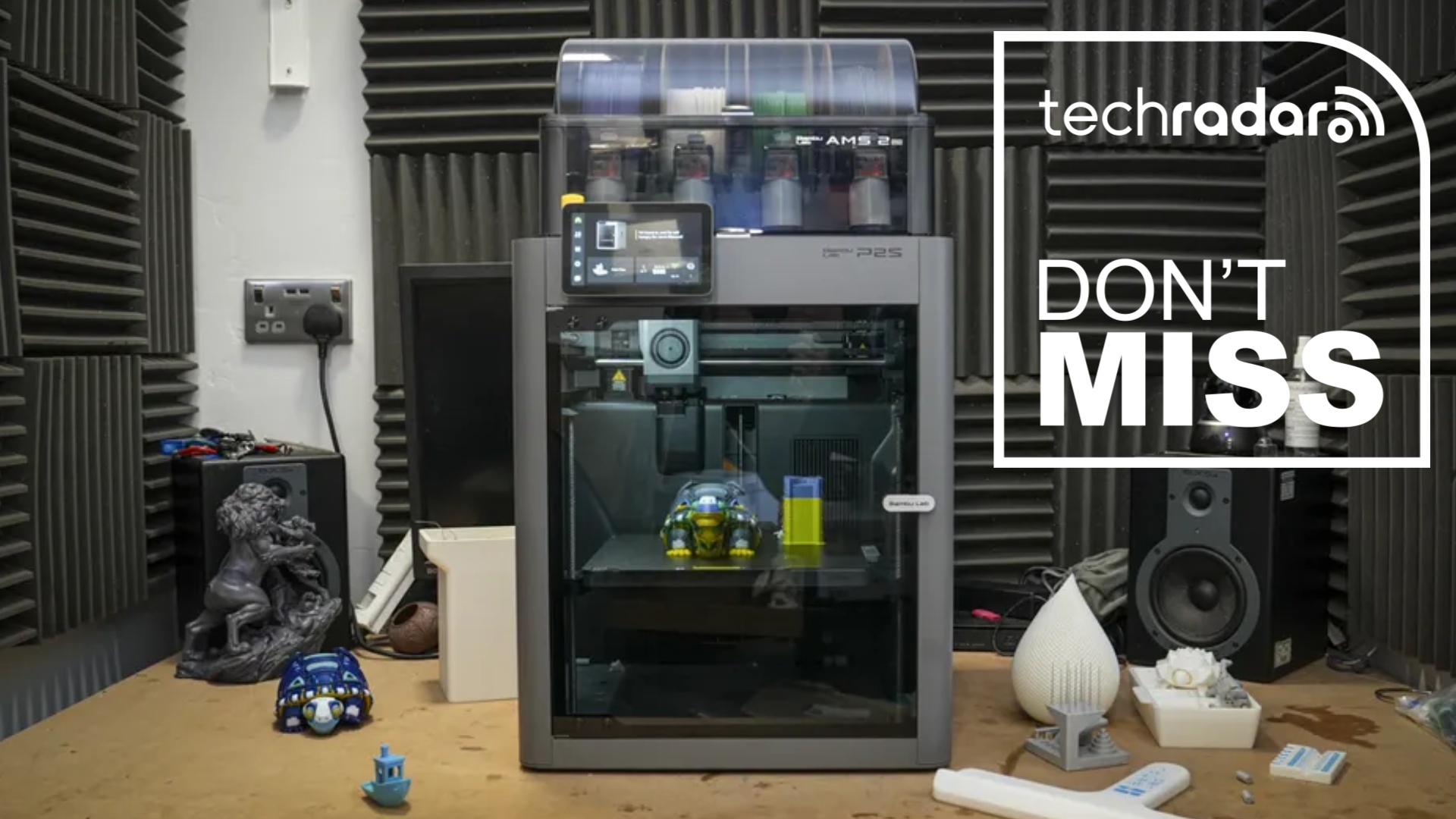 The Bambu Lab P2S 3D printer in our workshop under review, next to a white TechRadar badge in the upper right corner that reads 'Don't Miss'
