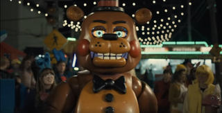 Freddy Fazbear standing in front of a crowd. He is an animatronic teddy bear with glowing blue eyes and a sinister look on his face.