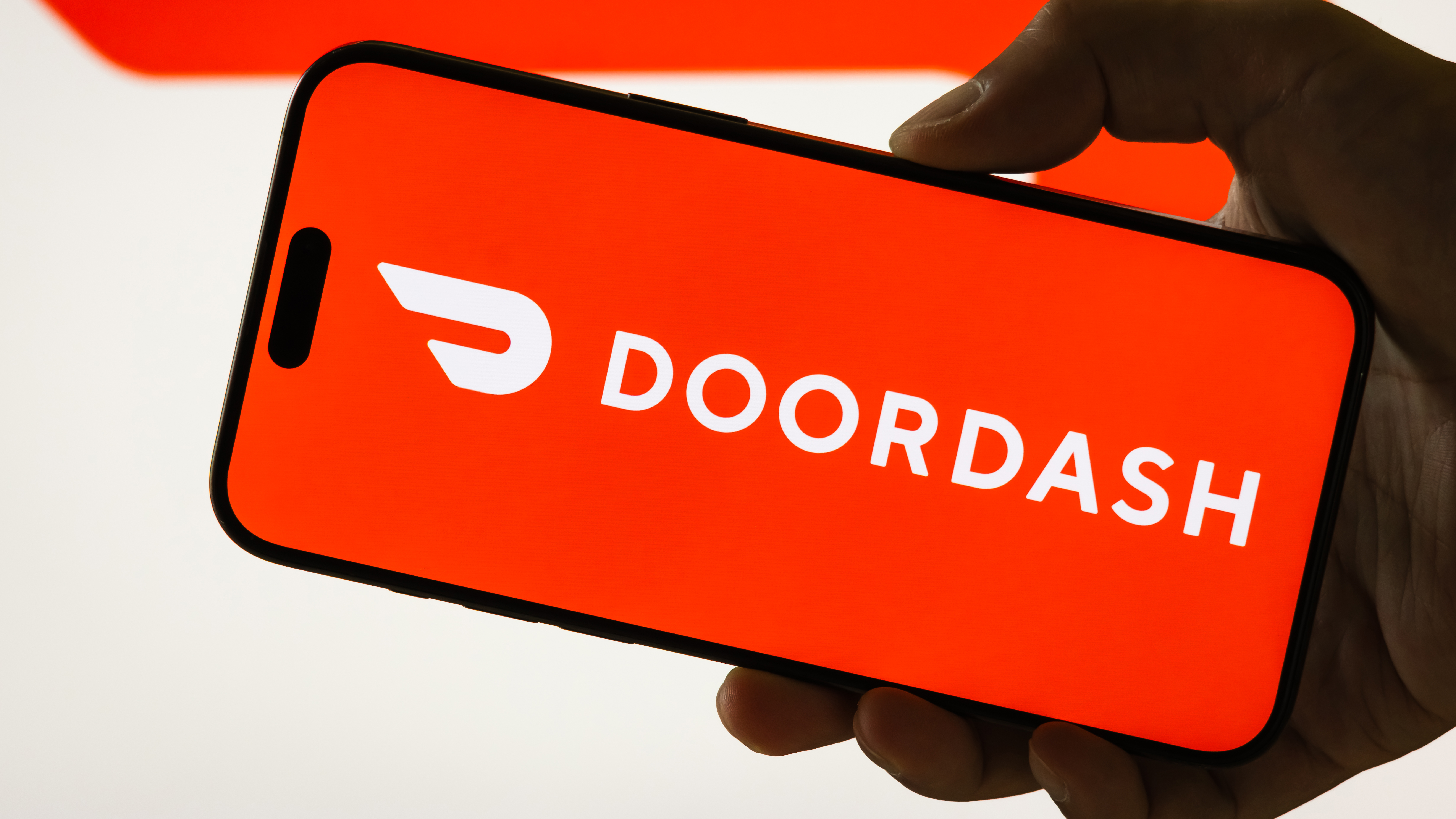 A hand holding a phone with the DoorDash logo