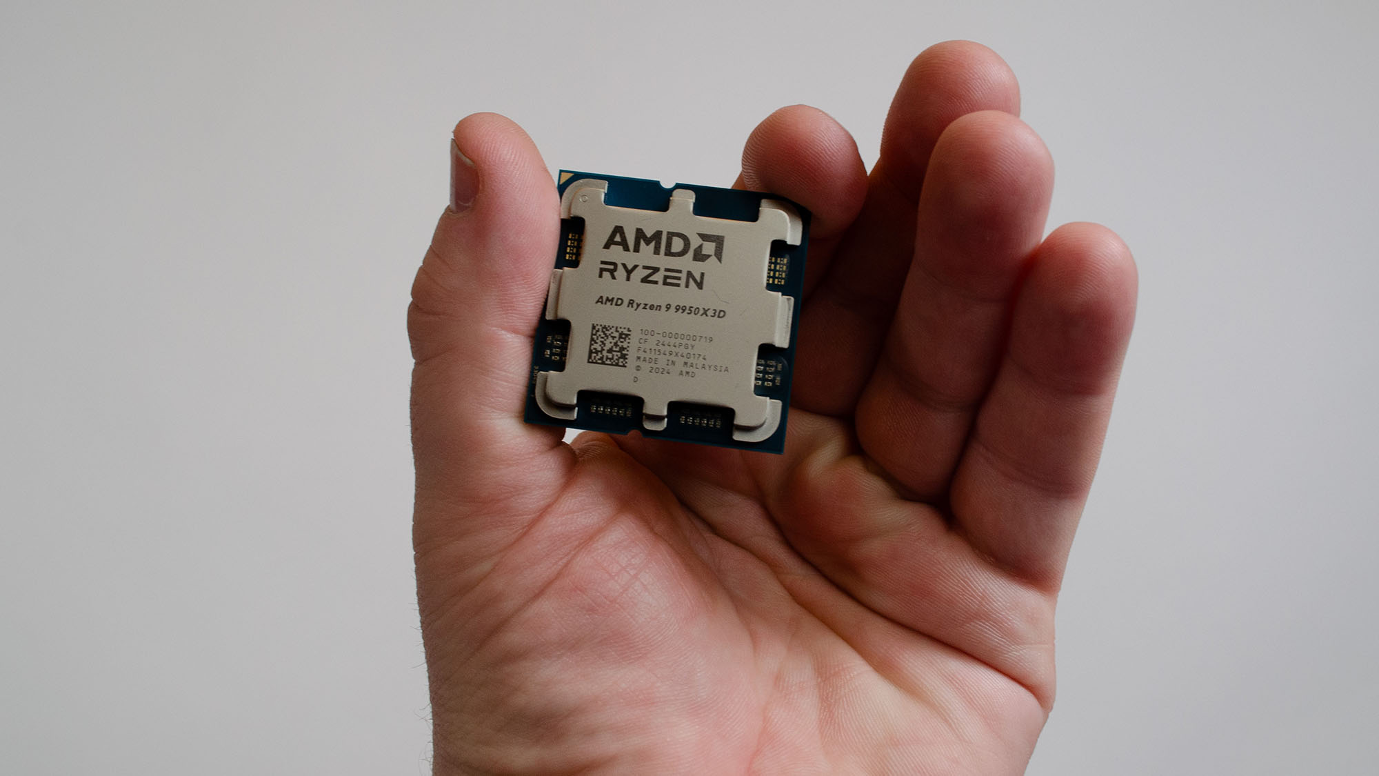 A masculine hand holding an AMD Ryzen 9 9950X3D processor
