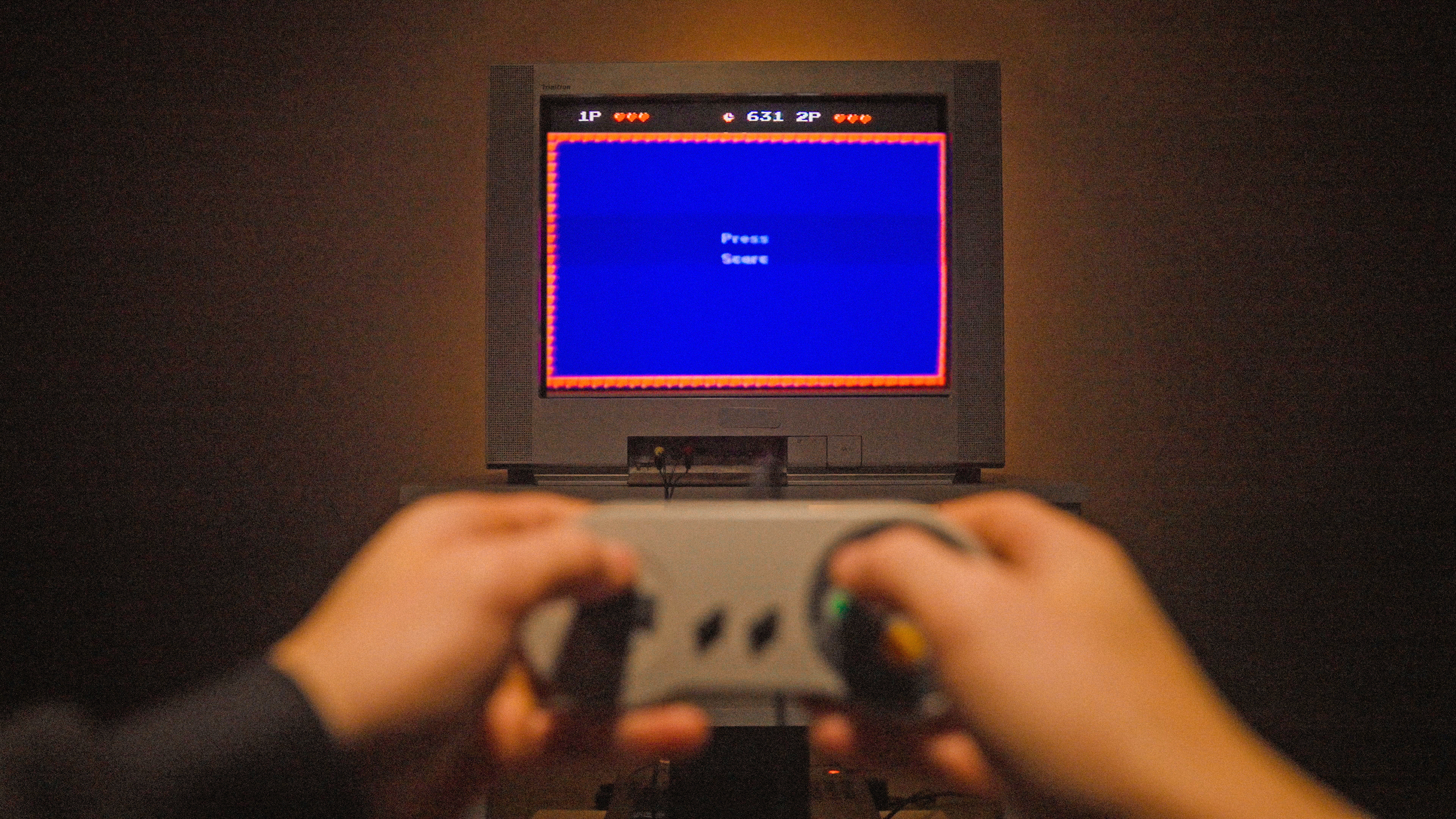 A pair of hands holds a SNES video game controller in front of a CRT TV with a screen saying Press Start