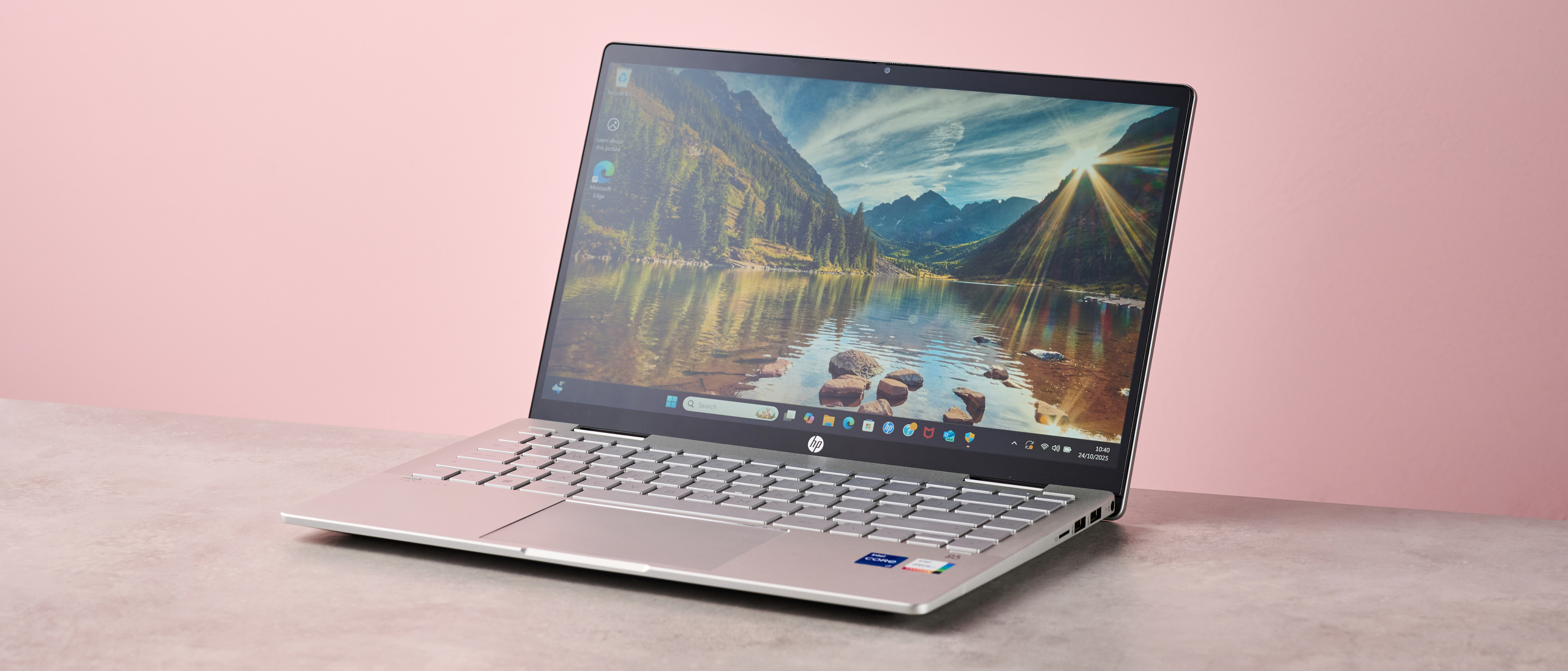 Three-quarter view of HP Pavilion x360 14 open on desk with pink wall in background 