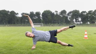 Leisure sports, personal fitness. A man is practicing a forearm stand on a sports field.