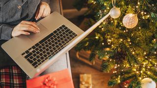 Close-up of a woman's hands with Christmas gifts, a coffee cup, and a laptop