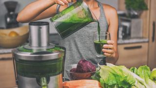 A woman making a healthy green juice in a juicer surrounded by vegetables