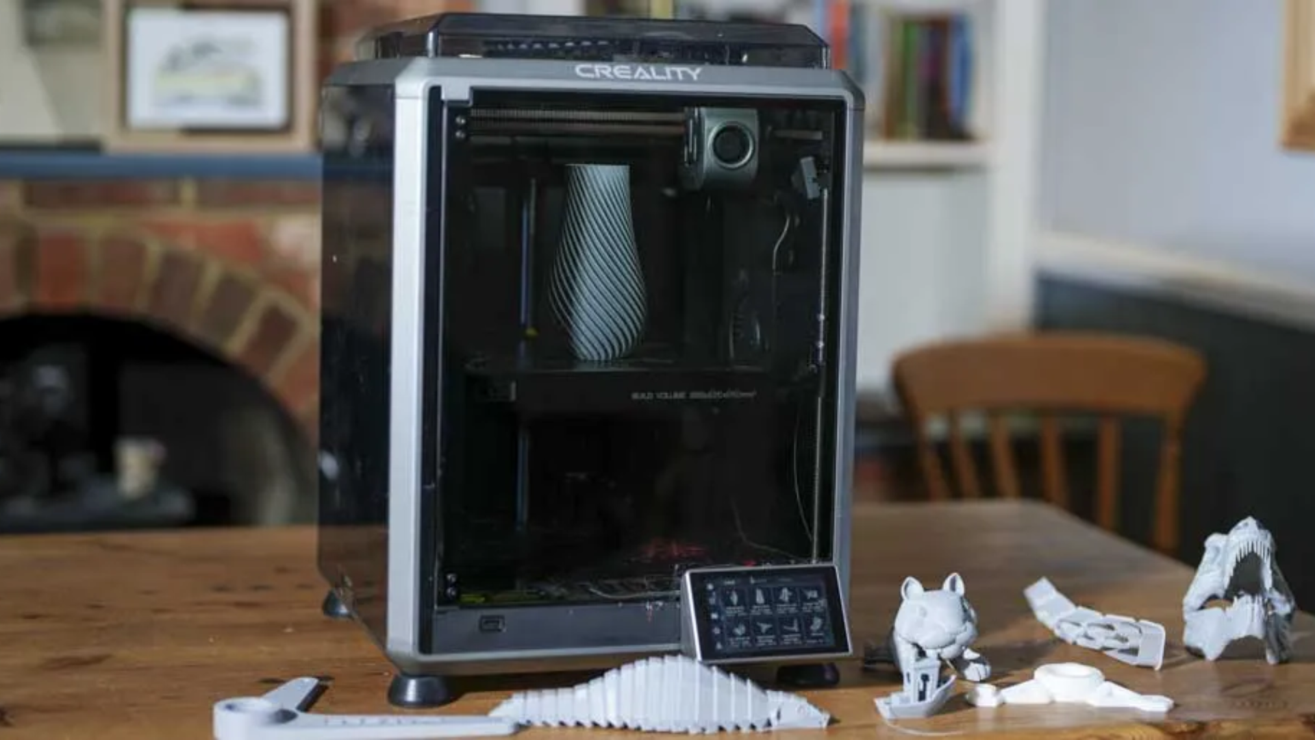 The Creality K1C on a table surrounded by dinoasaur 3D prints from our testing. A vase sits in the enclosure