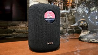WiiM Sound on a table, with wine glasses and a TV in the background
