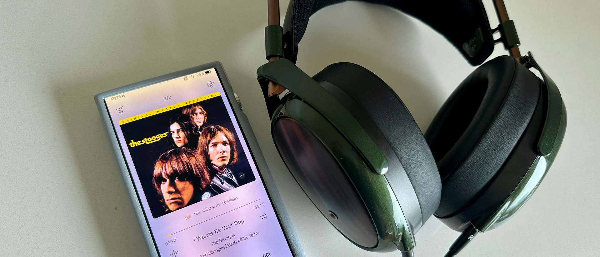 Meze Audi Strada over-ear headphones placed beside (and connected to) a DAP, showing music being played, on a white table