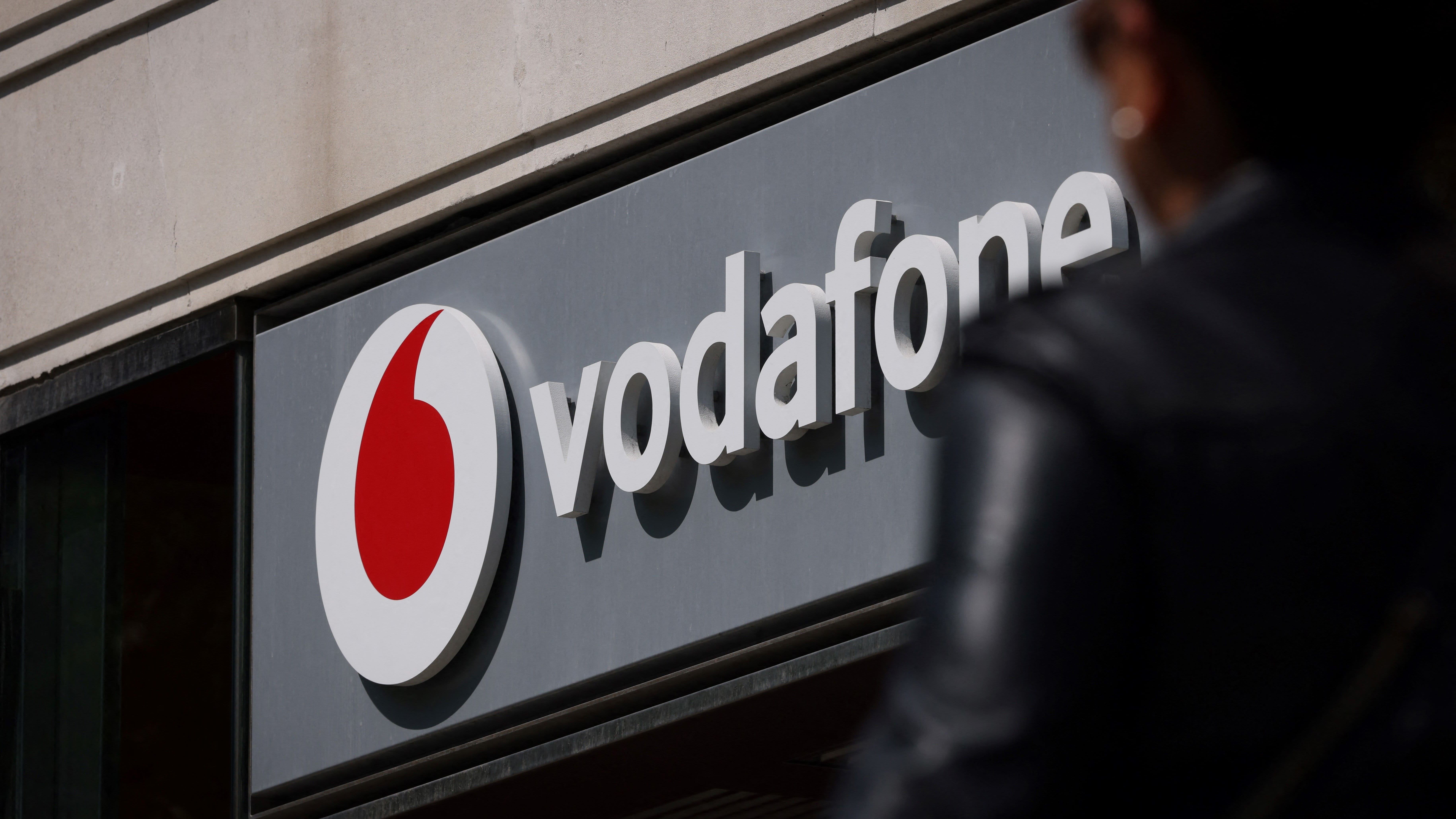 A person walking past the front of a Vodafone store, with the logo in large above the door