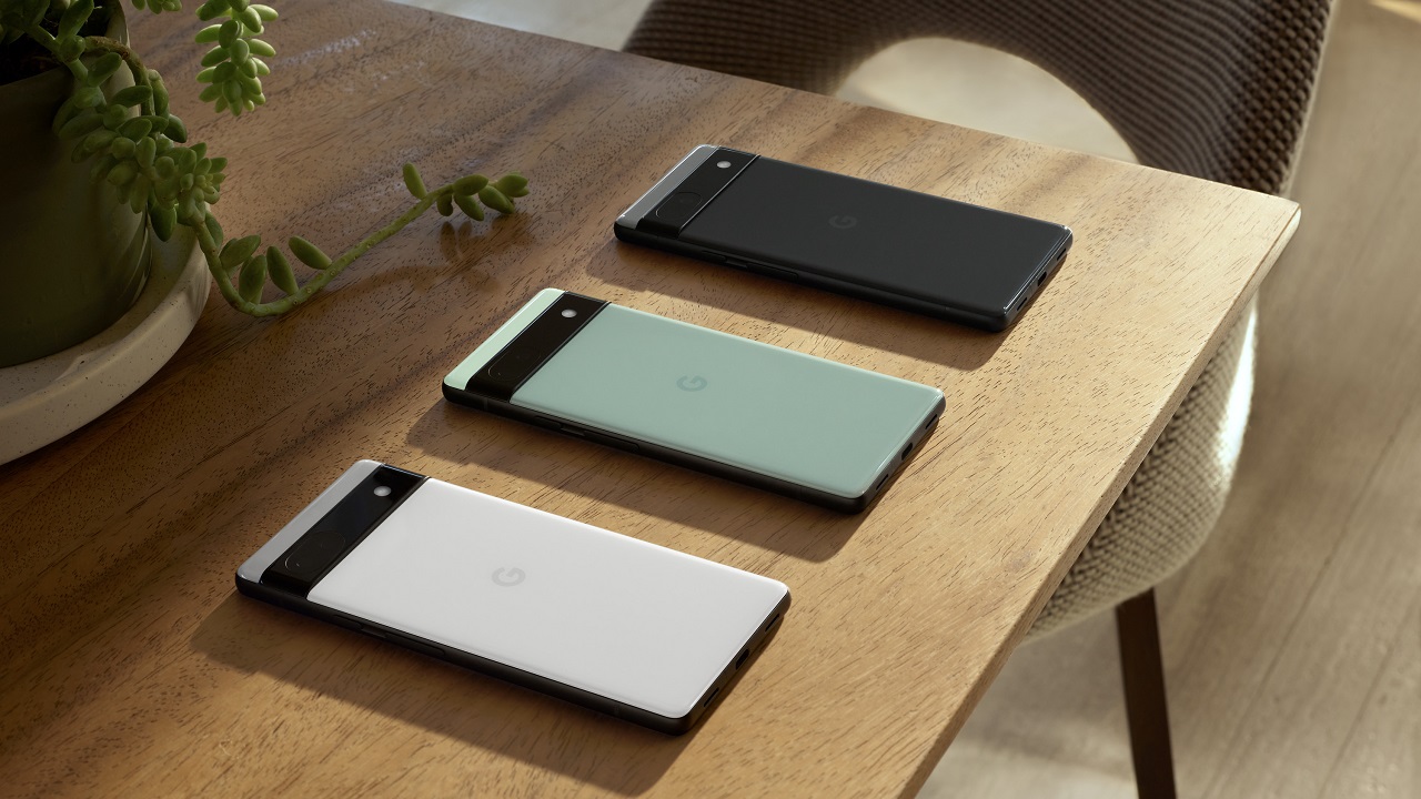Google Pixel 6a in chalk, sage and charcoal laying screen side down on a wooden table