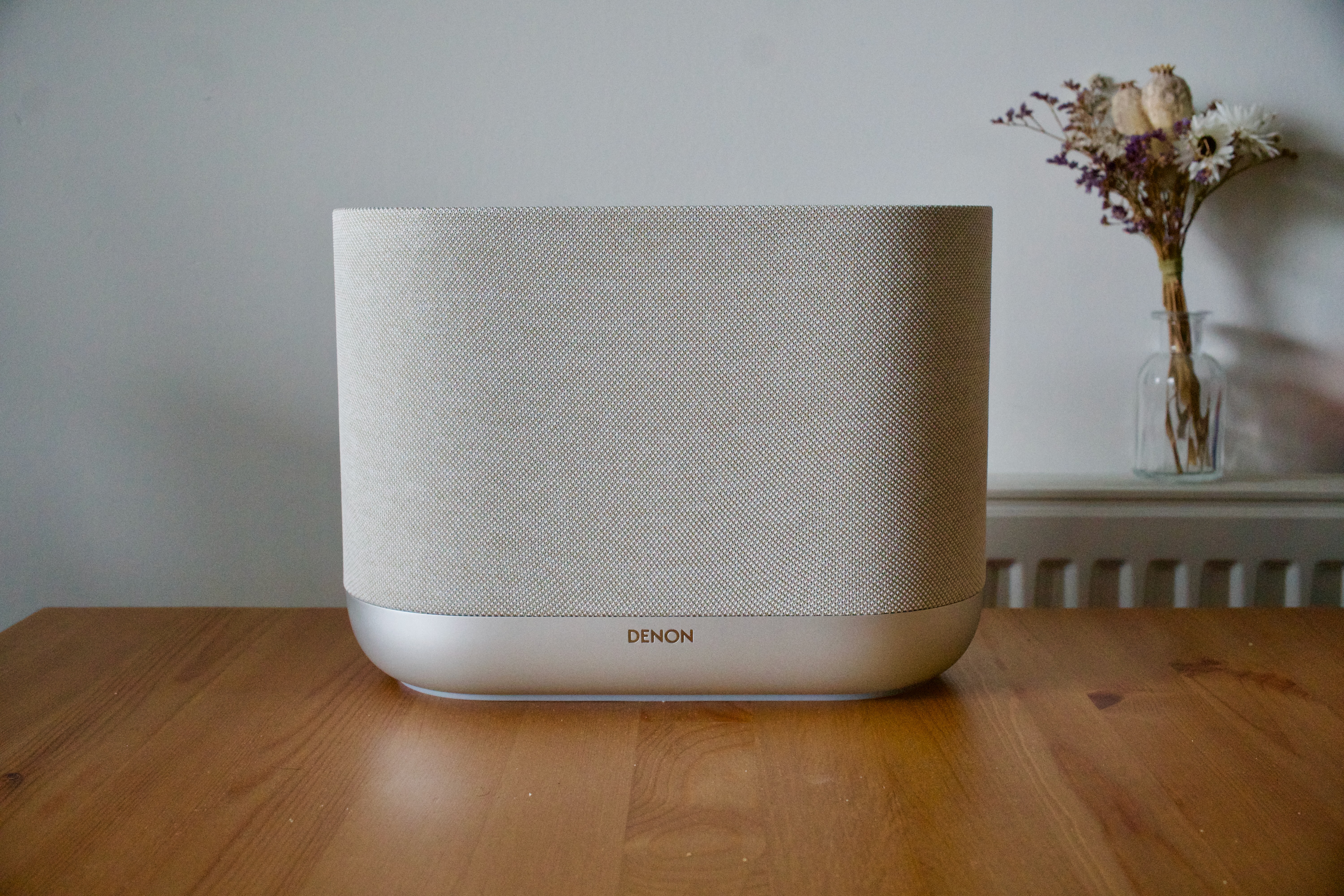 The white Denon Home 400 wireless home speaker on a wooden surface