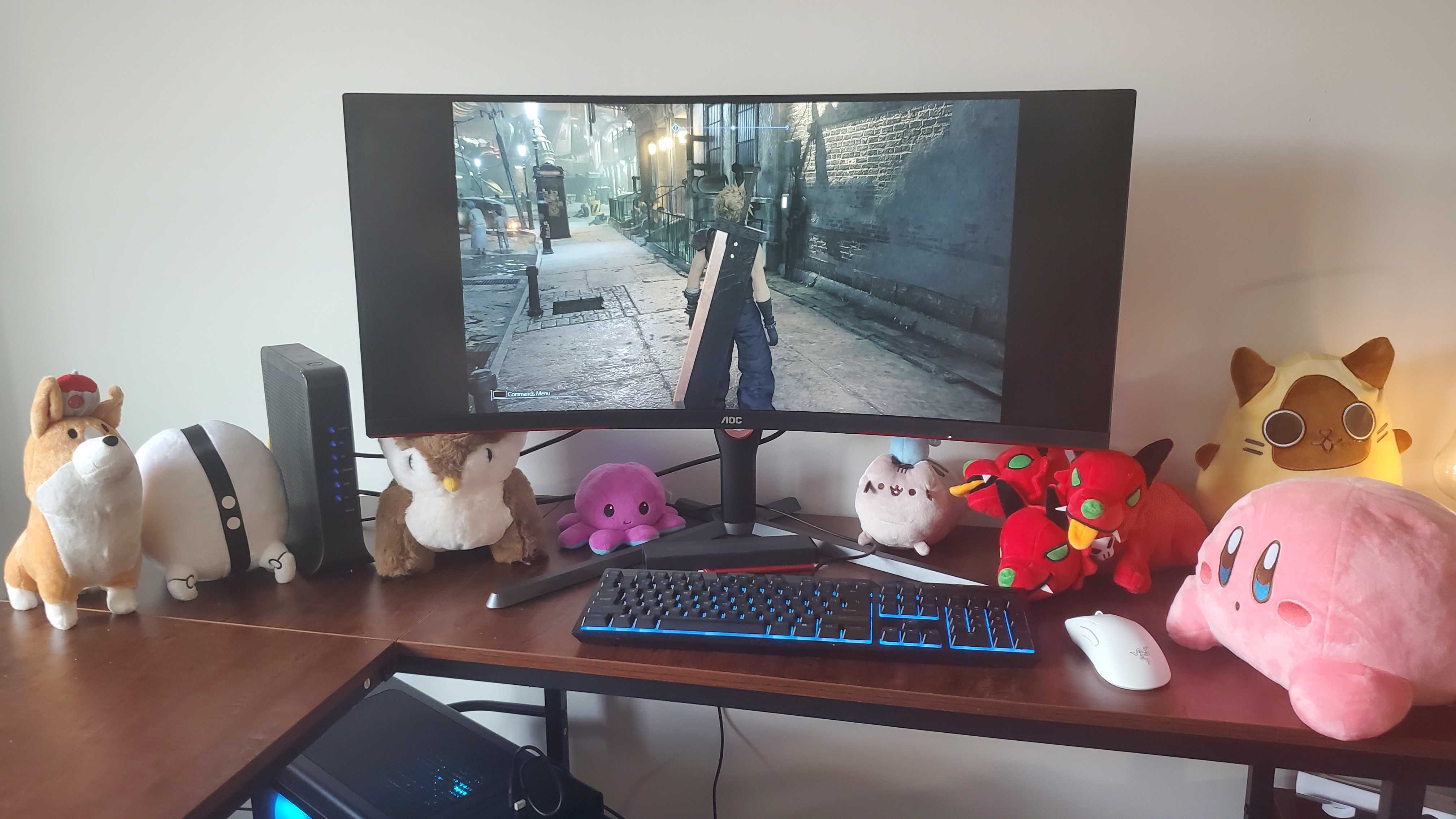 a large curved monitor on a wooden desk with several plushies under it